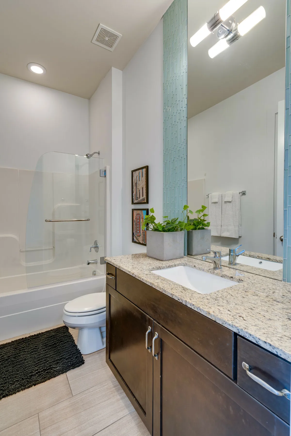 A calming bathroom setting showcasing a granite countertop, mirror, greenery, and framed artwork that enhance the soothing, spa-like atmosphere. The setup is ideal for both morning routines and unwinding after a long day.