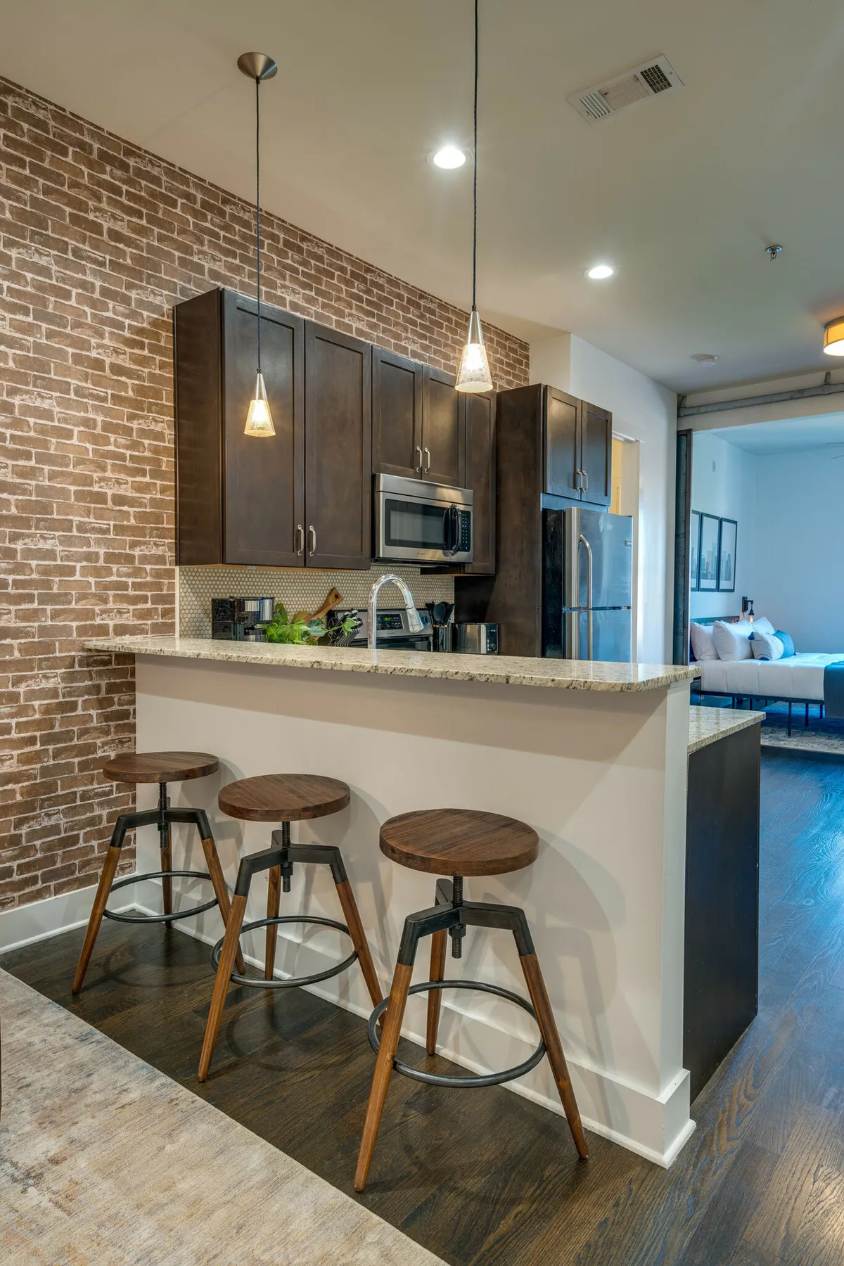 A modern laundry area and kitchen space with a brick wall, granite countertop, stools, and visible appliances. While primarily a kitchen, the inclusion of laundry amenities in the open-plan design speaks to the property’s practical perks.