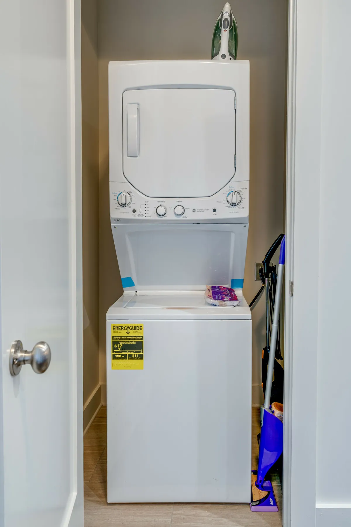 A practical laundry nook featuring a stacked washer and dryer, ironing board, and cleaning supplies. The space radiates organization and cleanliness, essential for a seamless and comfortable stay.