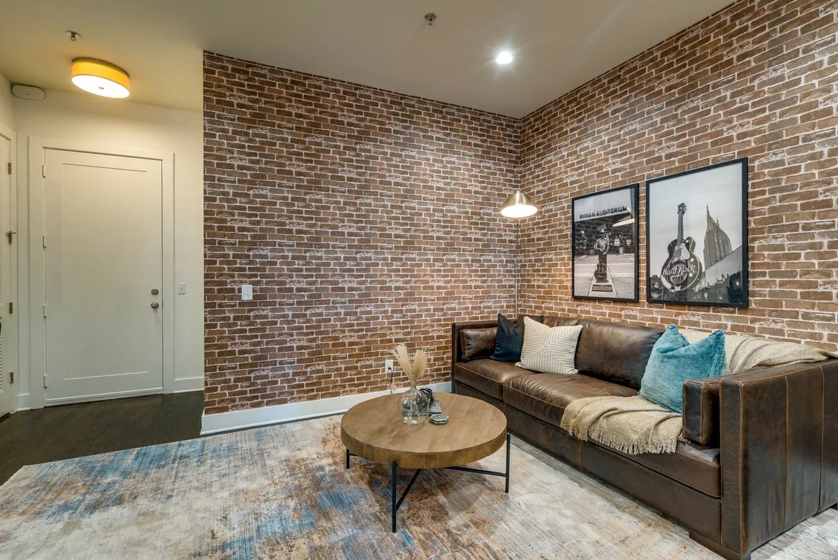 A stylish living space featuring a leather sofa, exposed brick wall, round coffee table, and eye-catching wall art. The setting encourages intimate conversations and cozy gatherings, embodying a modern loft vibe.