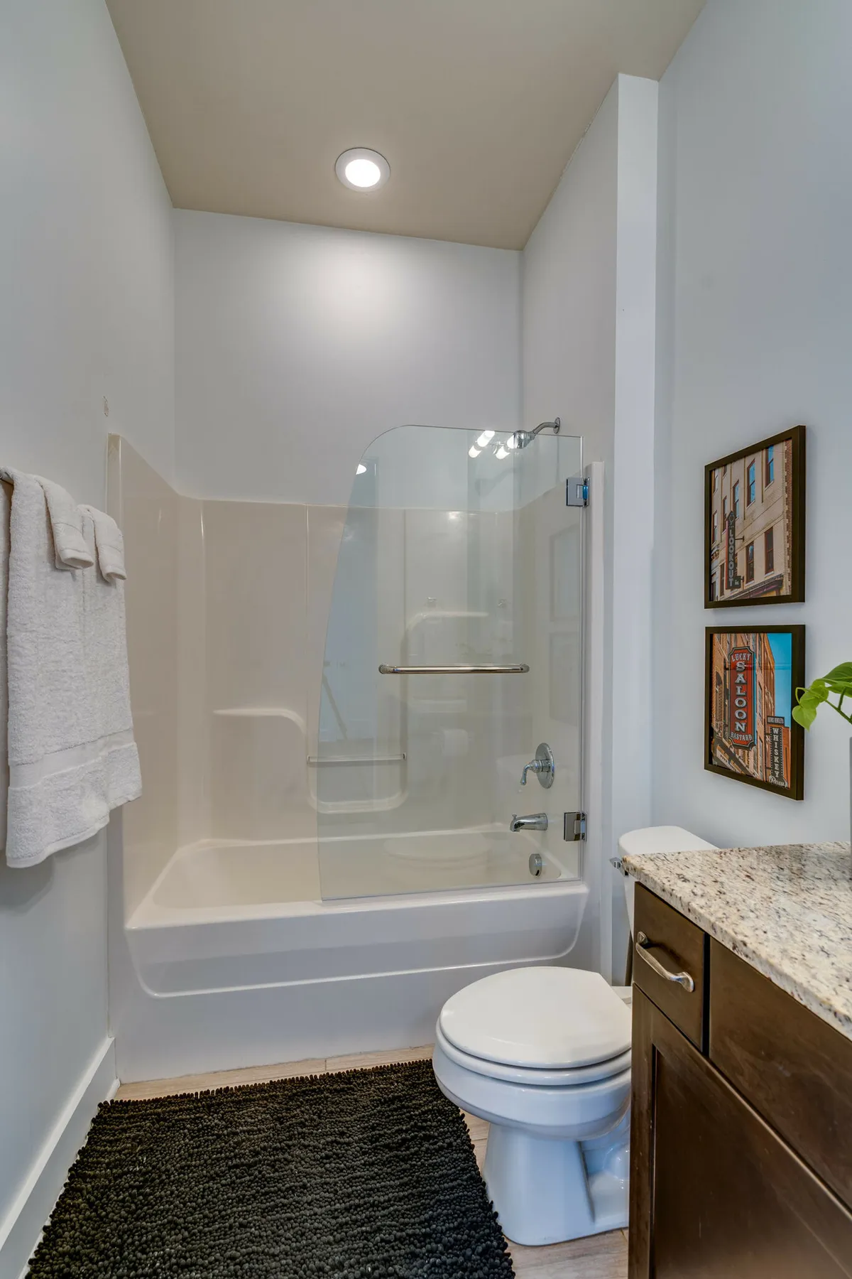 This image features a spa-inspired bathroom with a glass shower enclosure, granite countertop, framed art, and plush towels neatly arranged. The ambiance is inviting and refreshing, perfectly suited for relaxation and rejuvenation.